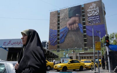 A woman walks past a billboard that shows a graphic depicting a military personnel's hand holding the Strait of Hormuz in his fist with signs which read in Farsi: 'In Iran's hands forever,' 'Trump couldn't do a damn thing,' and 'The control of Strait of Hormuz will be Iran's forever,' in Vanak Square, in northern Tehran, Iran, April 16, 2026. (AP/Vahid Salemi)