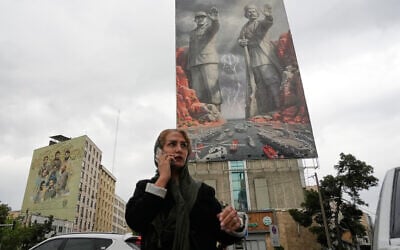 A woman talks on her cellphone as she walks past a billboard showing 20th century national hero Rais Ali Delvari, right, and slain IRGC navy chief Alireza Tangsiri, who was killed in the US-Israeli strike in late March 2026, on a building in Tehran, Iran, April 20, 2026. (AP Photo/Vahid Salemi)