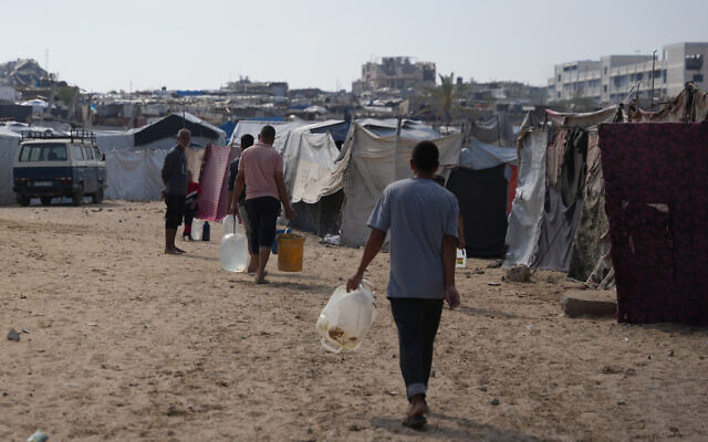Displaced Palestinian carry jerrycans filled with water through a tent camp in Khan Younis, in the southern Gaza Strip, Thursday, April 30, 2026. (AP Photo/Abdel Kareem Hana)