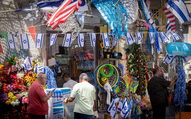 People outside a shop selling Israeli flags and other regalia, ahead of Israel's Independence Day, Shuk Levinsky in Tel Aviv, April 19, 2026. (Miriam Alster/FLASH90)