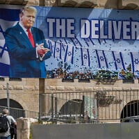 People walk next to a large billboard depicting US President Donald Trump with the slogan 'The Deliverer,' in Jerusalem, April 19, 2026. (Yonatan Sindel/Flash90)