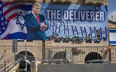 People walk next to a large billboard depicting US President Donald Trump with the slogan 'The Deliverer,' in Jerusalem, April 19, 2026. (Yonatan Sindel/Flash90)