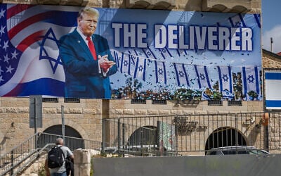 People walk next to a large billboard depicting US President Donald Trump with the slogan 'The Deliverer,' in Jerusalem, April 19, 2026. (Yonatan Sindel/Flash90)