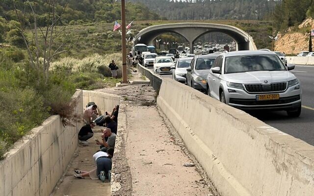 Travelers take shelter on the side of Route 1 near Shoeva, west of Jerusalem,  during an Iranian missile attack on April 6, 2026. (Sam Sokol/Times of Israel)