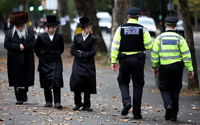 Members of the local Jewish community look on as Metropolitan Police officers patrol the streets in Stamford Hill, north London on October 2, 2025. (Henry Nicholls/AFP)