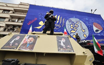 A member of Iran's security forces stands guard on an armored vehicle plastered with the pictures of, from left, Iran's slain supreme leader Ali Khamenei, his son and successor Mojtaba Khamenei and founding Supreme Leader Ruhollah Khomeini, during the funeral procession of Revolutionary Guard commanders killed in the regional war, on March 11, 2026. (Atta KENARE / AFP)