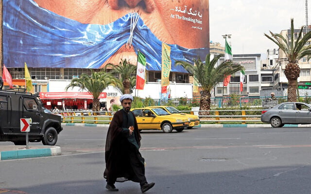 An Iranian cleric walks past an anti-US billboard referring to President Donald Trump and the Strait of Hormuz, installed on a building at the Valiasr Square in Tehran on May 2, 2026 (AFP)