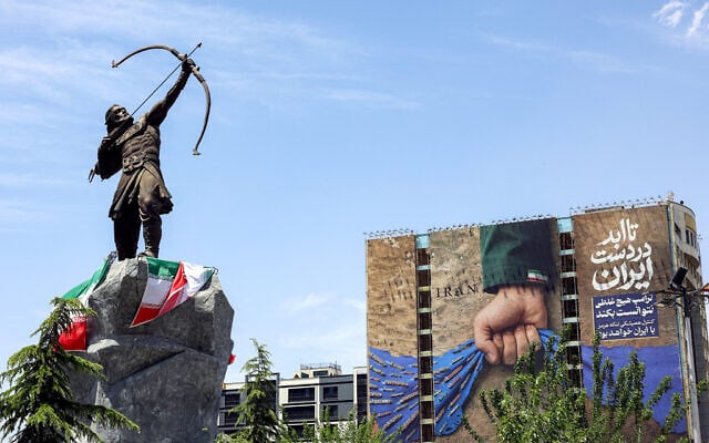 A statue depicting Persian mythical figure Arash the Archer, who according to tradition defined the border area between Persia and the Turanians, is displayed near a billboard on the facade of a building depicting the Strait of Hormuz with a caption in Persian reading "Forever in Iran's Hand", at Vanak Square in Tehran on May 6, 2026. (Photo by AFP)