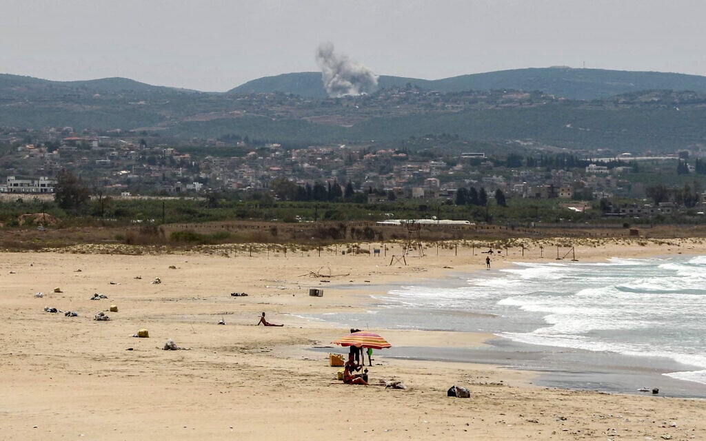 People sit along a beach in Tyre in southern Lebanon on May 17, 2026, as smoke billows behind them following strikes in the village of Zibqin. (Kawnat HAJU / AFP) People sit along a beach in Tyre in southern Lebanon on May 17, 2026, as smoke billows behind them following strikes in the village of Zibqin. (Kawnat HAJU / AFP)