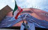 A man waves an Iranian flag for a pro-government campaign under a billboard with a graphic showing the Strait of Hormuz and sewn lips of US President Donald Trump in a square in downtown Tehran, May 6, 2026. (AP Photo/Vahid Salemi)