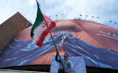 A man waves an Iranian flag for a pro-government campaign under a billboard with a graphic showing the Strait of Hormuz and sewn lips of US President Donald Trump in a square in downtown Tehran, May 6, 2026. (AP Photo/Vahid Salemi)