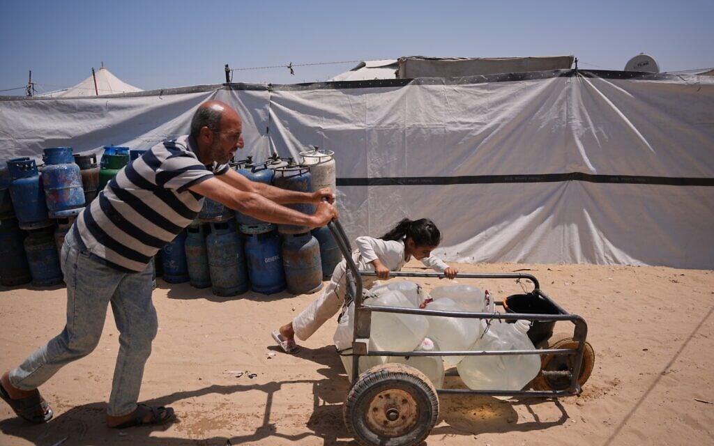 Ne'man Abu Jarad and his daughter push a cart loaded with jerrycans filled with water as they walk at a tent camp for displaced Palestinians in Khan Younis, southern Gaza Strip, on May 13, 2026. (AP Photo/Abdel Kareem Hana)