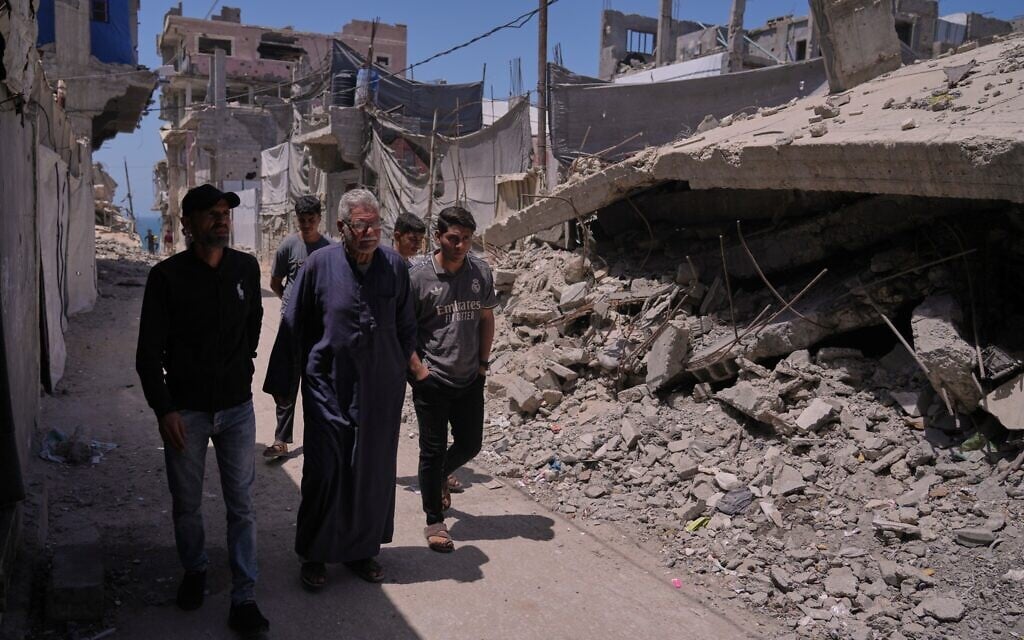 Palestinian Yusuf Abu Hamam, front center, walks with his grandchildren and son past buildings destroyed during Israeli air and ground operations in the Shati refugee camp in Gaza City, on May 13, 2026. (AP Photo/Jehad Alshrafi)