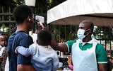 A health official uses a thermometer to screen people in front of Kibuli Muslim Hospital in Kampala, Uganda, May 16, 2026. (Hajarah Nalwadda/AP)