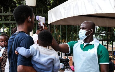 A health official uses a thermometer to screen people in front of Kibuli Muslim Hospital in Kampala, Uganda, May 16, 2026. (Hajarah Nalwadda/AP)