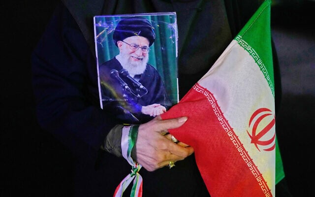 A demonstrator holds a poster of the slain Iranian Supreme Leader Ayatollah Ali Khamenei, and an Iranian flag during a pro-government gathering at a square in downtown Tehran, Iran, May 19, 2026. (AP Photo/Vahid Salemi)