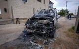 A man stands near a burned car and graffiti on a mosque wall, which Palestinians say was made by extremist Israeli settlers, in the village of Jibya, north of Ramallah in the West Bank, May 15, 2026. (Flash90)