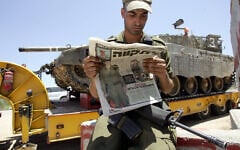An Israeli soldier reads a newspaper with a picture of Gilad Shalit as a tank prepares to deploy near the Gaza border on June 26, 2006. (AFP/MENAHEM KAHANA)