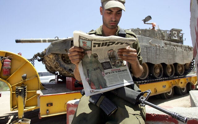 An Israeli soldier reads a newspaper with a picture of Gilad Shalit as a tank prepares to deploy near the Gaza border on June 26, 2006. (AFP/MENAHEM KAHANA) An Israeli soldier reads a newspaper with a picture of Gilad Shalit as a tank prepares to deploy near the Gaza border on June 26, 2006. (AFP/MENAHEM KAHANA)