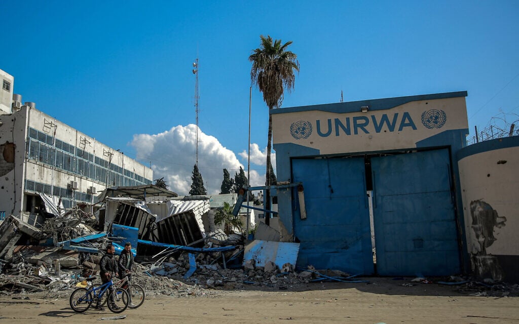 Two Palestinians walks with their bicycles past past the damaged Gaza City headquarters of the United Nations Relief and Works Agency for Palestine Refugees (UNRWA) on February 15, 2024 (AFP)
