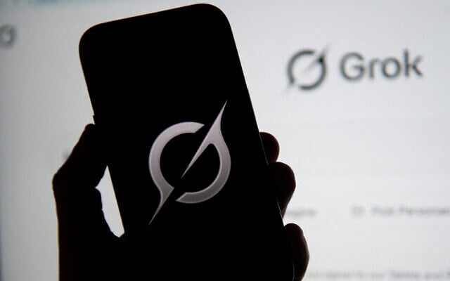 In this photo illustration, the Grok logo is seen on a mobile phone next to the website displayed on a computer screen in Bogota on February 12, 2026. (Pablo Vera/AFP)