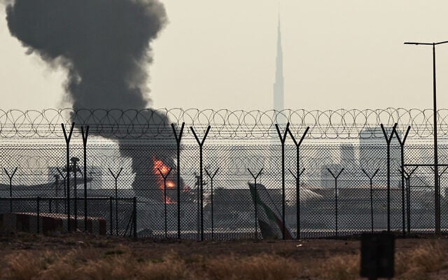 The Dubai skyline with the landmark Burj Khalifa skyscraper (R) is pictured as a smoke plume rises from an ongoing fire near Dubai International Airport on March 16, 2026. (AFP)