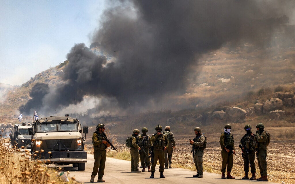Israeli security forces stand guard along a road while behind smoke billows from an area reportedly set ablaze by Israeli settlers in the Palestinian village of Idna, west of Hebron in the West Bank, on June 5, 2026. (HAZEM BADER / AFP)