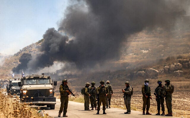 Israeli security forces stand guard along a road while behind smoke billows from an area reportedly set ablaze by Israeli settlers in the Palestinian village of Idna, west of Hebron in the West Bank, on June 5, 2026. (HAZEM BADER / AFP) Israeli security forces stand guard along a road while behind smoke billows from an area reportedly set ablaze by Israeli settlers in the Palestinian village of Idna, west of Hebron in the West Bank, on June 5, 2026. (HAZEM BADER / AFP)