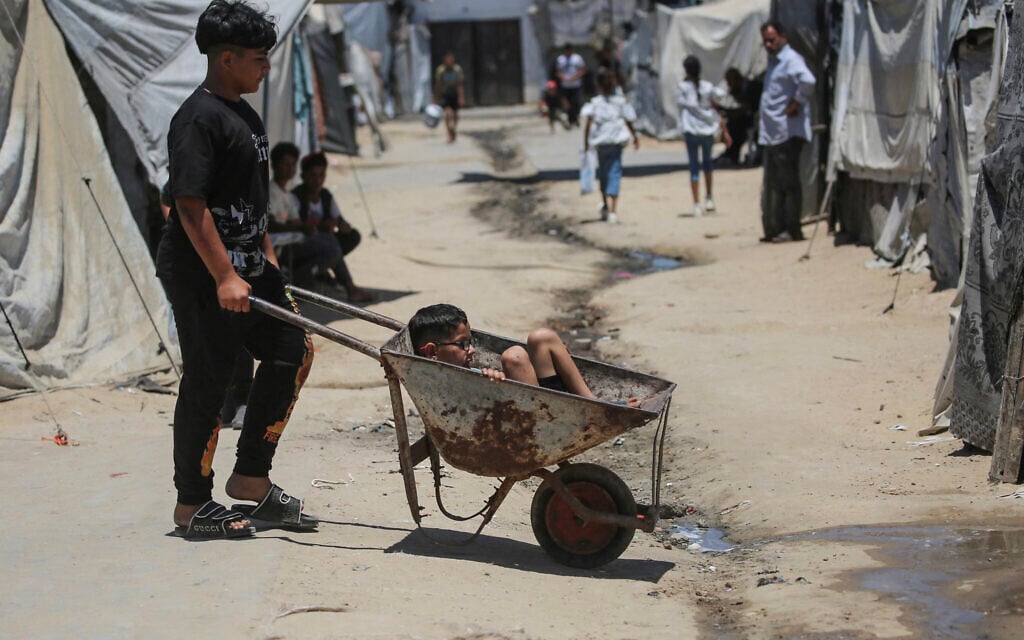 A Palestinian boy transports another child in a wheelbarrow amid makeshift shelters in Gaza's Nuseirat refugee camp on June 11, 2026. (Eyad Baba / AFP)