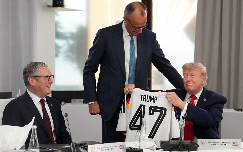 US President Donald Trump (R) reacts as he holds up a jersey of Germany's national football team bearing the number 47 and his name, gifted by Germany's Chancellor Friedrich Merz (C) flanked by Britain's Prime Minister Keir Starmer ahead of a working session at the G7 summit in Evian-les-Bains, central-eastern France on June 16, 2026. (Thibault Camus / POOL / AFP)