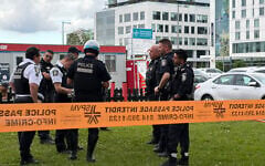 Damaged windows can be seen in the distance as police gather near the scene of a shooting in Montreal on June 22, 2026, which left two people and the attacker dead. (Daphné LEMELIN / AFP)