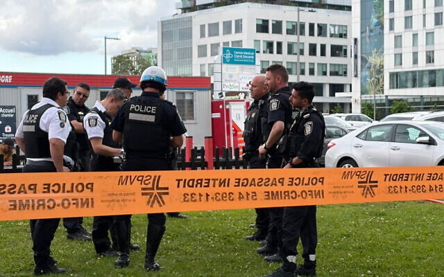 Damaged windows can be seen in the distance as police gather near the scene of a shooting in Montreal on June 22, 2026, which left two people and the attacker dead. (Daphné LEMELIN / AFP)