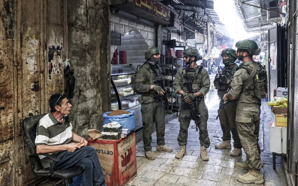 A Palestinian man sits outside a shop as Israeli soldiers patrol the market in the Old City of Nablus in the northern West Bank on June 23, 2026 (JAAFAR ASHTIYEH / AFP)