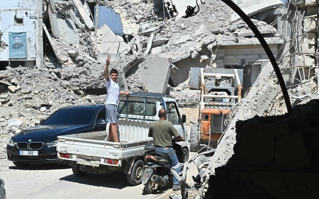 A Lebanese boy flashes the victory sign as he stands in the back of a truck driving past the rubble of destroyed homes and businesses following Israeli military strikes. in the southern Lebanese village of Srifa on June 24, 2026. (FADEL itani / AFP) /