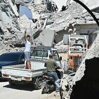 A Lebanese boy flashes the victory sign as he stands in the back of a truck driving past the rubble of destroyed homes and businesses following Israeli military strikes. in the southern Lebanese village of Srifa on June 24, 2026. (FADEL itani / AFP) /