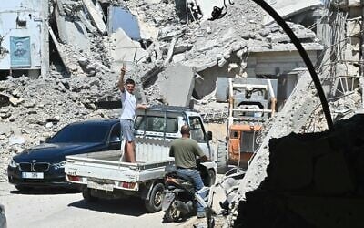 A Lebanese boy flashes the victory sign as he stands in the back of a truck driving past the rubble of destroyed homes and businesses following Israeli military strikes. in the southern Lebanese village of Srifa on June 24, 2026. (FADEL itani / AFP) /