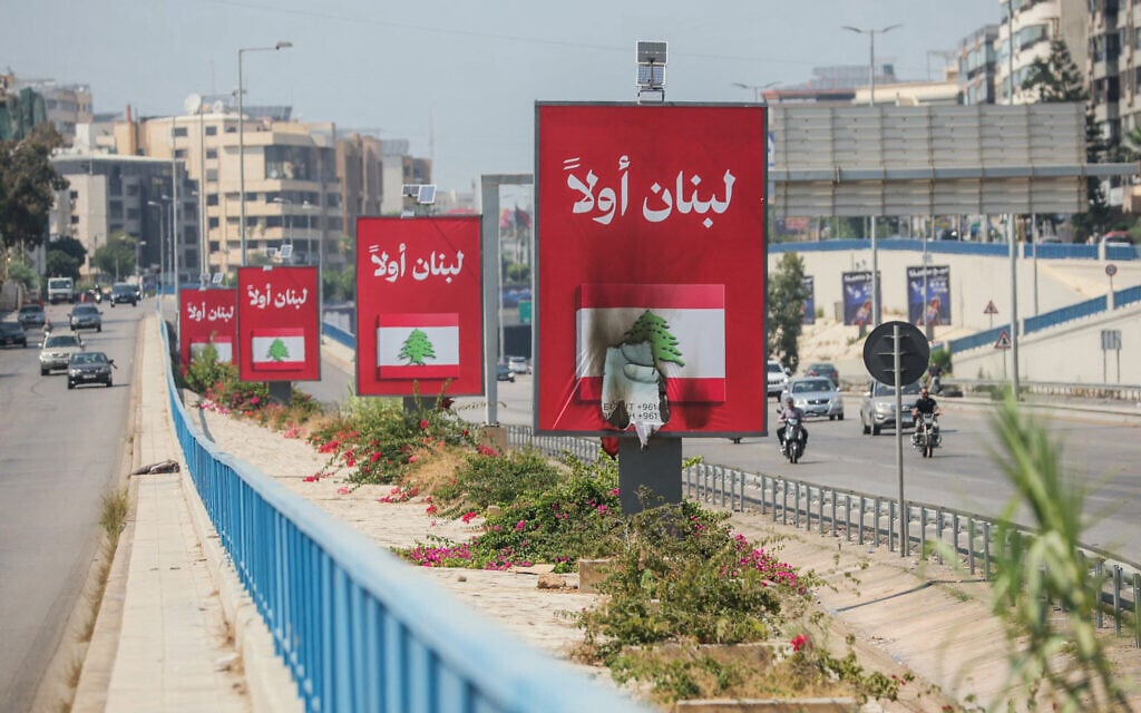 Vehicles drive past billboards that read in Arabic, 'Lebanon first,' one of which was set on fire along Beirut's airport road near Tehran-backed Hezbollah's stronghold, amidst tensions following Lebanon's framework agreement with Israel on June 28, 2026 (ibrahim AMRO / AFP)