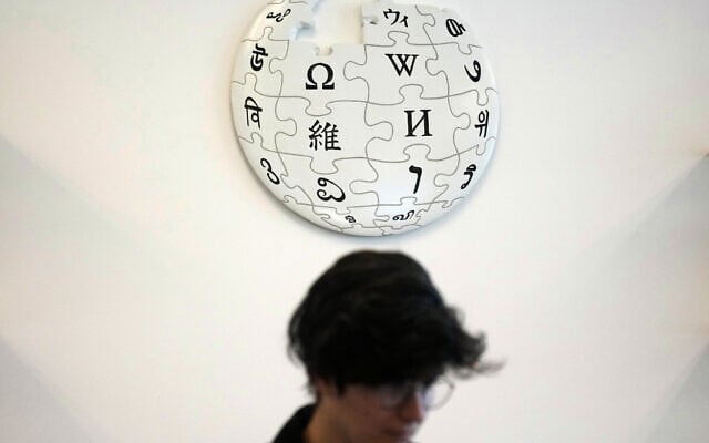 A volunteer Wikipedia editor sits below a Wikipedia logo displayed at the Wikimedia Foundation office in San Francisco, California, January 12, 2026. (AP Photo/Jeff Chiu)