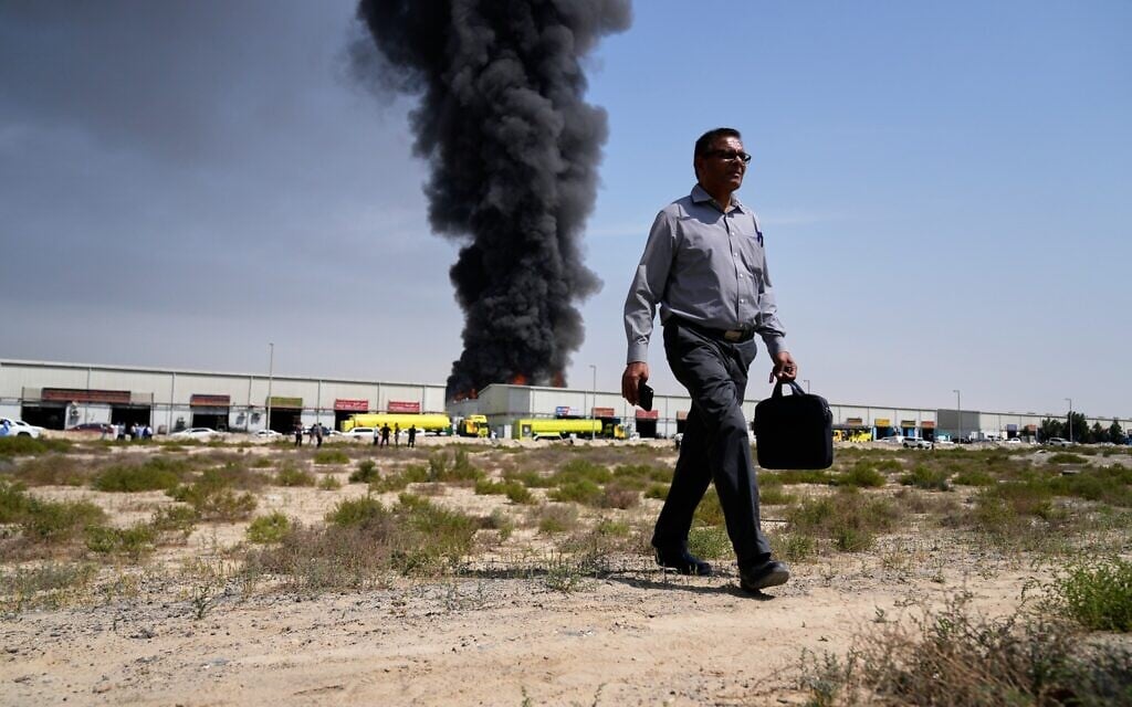 A man walks away after watching as a black plume of smoke rises from a warehouse in the industrial area of Sharjah City, United Arab Emirates, March 1, 2026, following Iranian strikes. (AP Photo/Altaf Qadri)