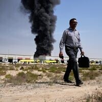 A man walks away after watching as a black plume of smoke rises from a warehouse in the industrial area of Sharjah City, United Arab Emirates, March 1, 2026, following Iranian strikes. (AP Photo/Altaf Qadri)