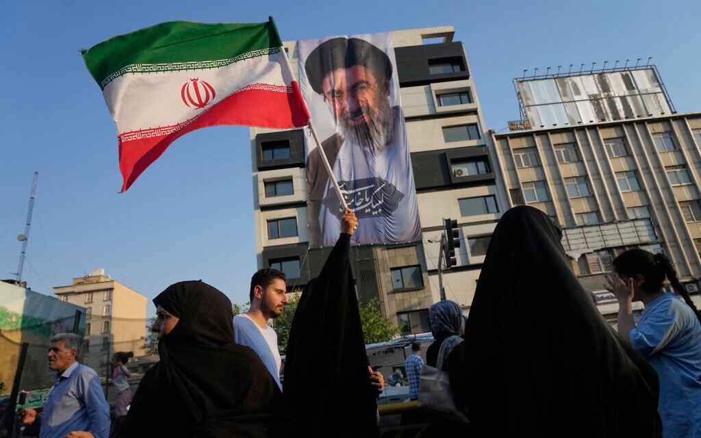 A woman holds up an Iranian flag in front of a banner showing a portrait of the Supreme Leader Ayatollah Mojtaba Khamenei, during a street festival celebrating the Muslim Shiite holiday of Eid al-Ghadir, in Tehran, Iran, June 4, 2026. (AP Photo/Vahid Salemi)