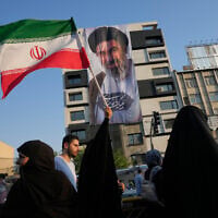 A woman holds up an Iranian flag in front of a banner showing a portrait of Supreme Leader Ayatollah Mojtaba Khamenei during a street festival celebrating the Muslim Shiite holiday of Eid al-Ghadir in Tehran, Iran, June 4, 2026. (AP/Vahid Salemi)