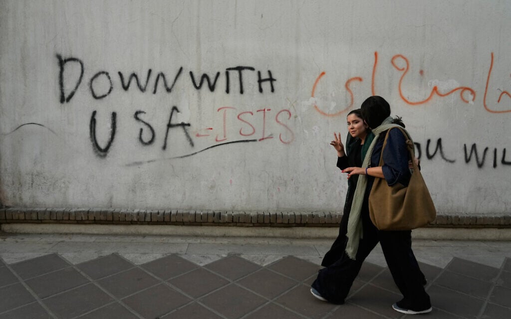 A woman reacts to the camera as she walks past an anti-US graffiti painted on the wall of the British Embassy in Tehran, Iran, June 6, 2026. (AP Photo/Vahid Salemi)