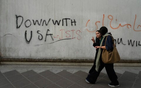 A woman reacts to the camera as she walks past an anti-US graffiti painted on the wall of the British Embassy in Tehran, Iran, June 6, 2026. (AP Photo/Vahid Salemi)