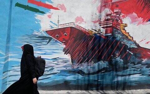 A woman walks past a mural depicting a US aircraft carrier under missile attack in downtown Tehran, Iran,, June 8, 2026. (AP Photo/Vahid Salemi)