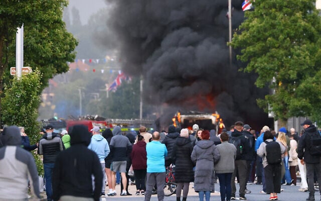People watch as a vehicle burns during a protest following a stabbing incident in North Belfast, June 9, 2026. (AP/Peter Morrison) People watch as a vehicle burns during a protest following a stabbing incident in North Belfast, June 9, 2026. (AP/Peter Morrison)