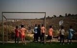 Palestinian boys look toward a young Israeli settler after their soccer ball, kicked beyond a barbed-wire fence surrounding a small pitch near the Carmel settlement, was taken away in the West Bank Bedouin village of Umm al-Khair, May 12, 2026. (AP Photo/Leo Correa)