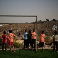 Palestinian boys look toward a young Israeli settler after their soccer ball, kicked beyond a barbed-wire fence surrounding a small pitch near the Carmel settlement, was taken away in the West Bank Bedouin village of Umm al-Khair, May 12, 2026. (AP Photo/Leo Correa)