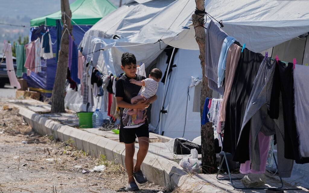 A displaced boy who fled his village with his family in south Lebanon, carries a child as he walks outside their tents at an alley in the southern port city of Sidon, Lebanon, June 10, 2026. (AP Photo/Mohammed Zaatari)