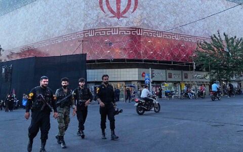 Policemen walk in front of a banner of the Iranian flag in the Islamic Revolution Square in Tehran, Iran, June 14, 2026. (AP/Vahid Salemi)